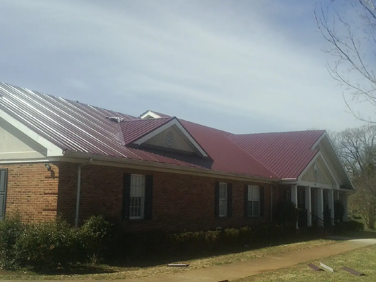 Red metal roof with gabled entries on a long brick building, from a Hail Damage Roof Repair job in Warriors Mark