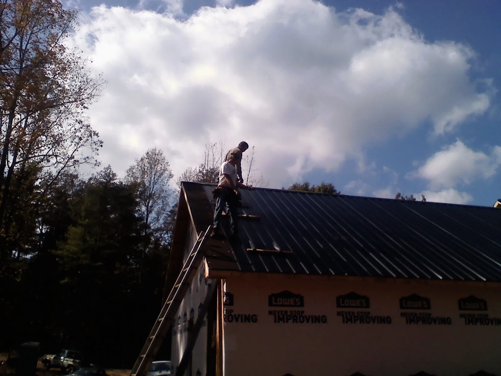 Roofer fastening dark metal panels high against a cloudy sky, from a Roof Inspection job in Warriors Mark