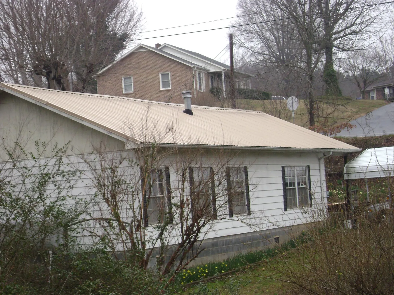 Tan metal roof on a white sided house set into a hillside — Commercial Roofing by Roofing Brothers in Warriors Mark
